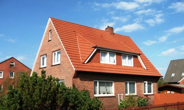 A two-story house with a red roof, brick walls, and a wooden fence.