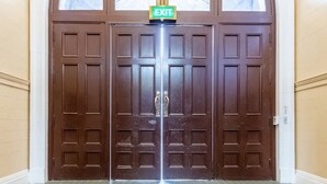 Une porte à deux battants surmontée d’un panneau indiquant « SORTIE », qui donne sur un couloir au revêtement de sol à motifs.