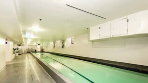 Une longue et étroite piscine intérieure, dont le sol et les murs sont recouverts de carreaux, et dont le plafond est doté d’un éclairage encastré.