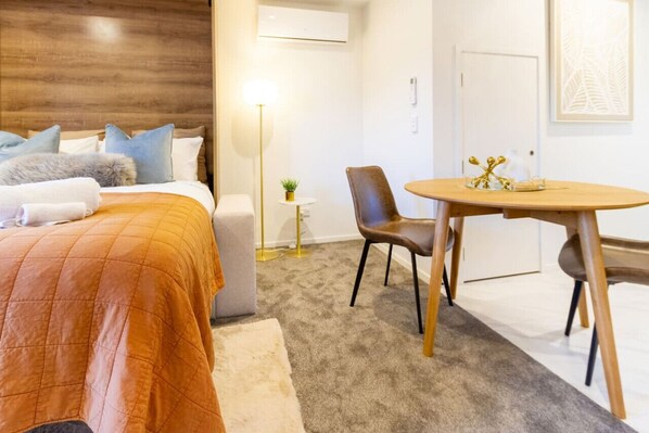 A hotel room with a bed, a chair, a small table, and a lamp.