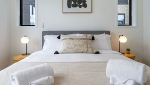 Una cama bien hecha con sábanas blancas, cabecera gris y dos lámparas de noche.