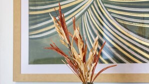 Una mesa de comedor con un jarrón de plantas secas, un cuadro abstracto enmarco y sillas verdes.