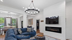 A modern living room with a sectional sofa, a fireplace, a TV mounted on the wall, and a chandelier. - Lakefront Bliss - Fully Loaded (Eatonton)