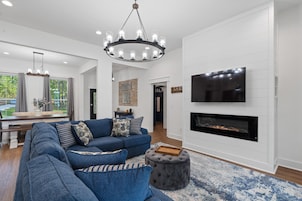 A modern living room with a sectional sofa, a fireplace, a TV mounted on the wall, and a chandelier.