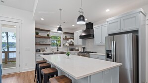 A modern kitchen with a large island, stainless steel appliances, and wooden bar stools. - Lakefront Bliss - Fully Loaded (Eatonton)