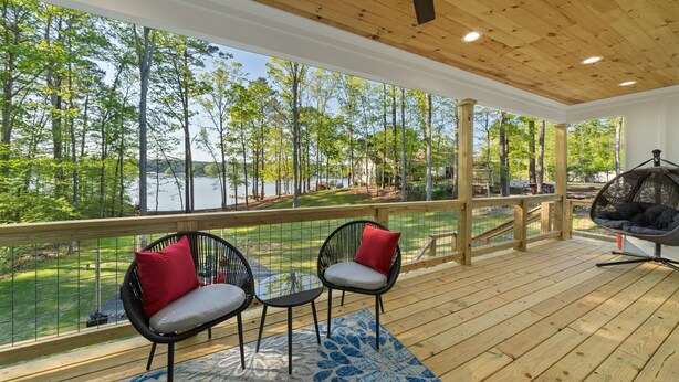 A wooden deck with two chairs and a hanging chair, overlooking a lake and trees. - Lakefront Bliss - Fully Loaded (Eatonton)