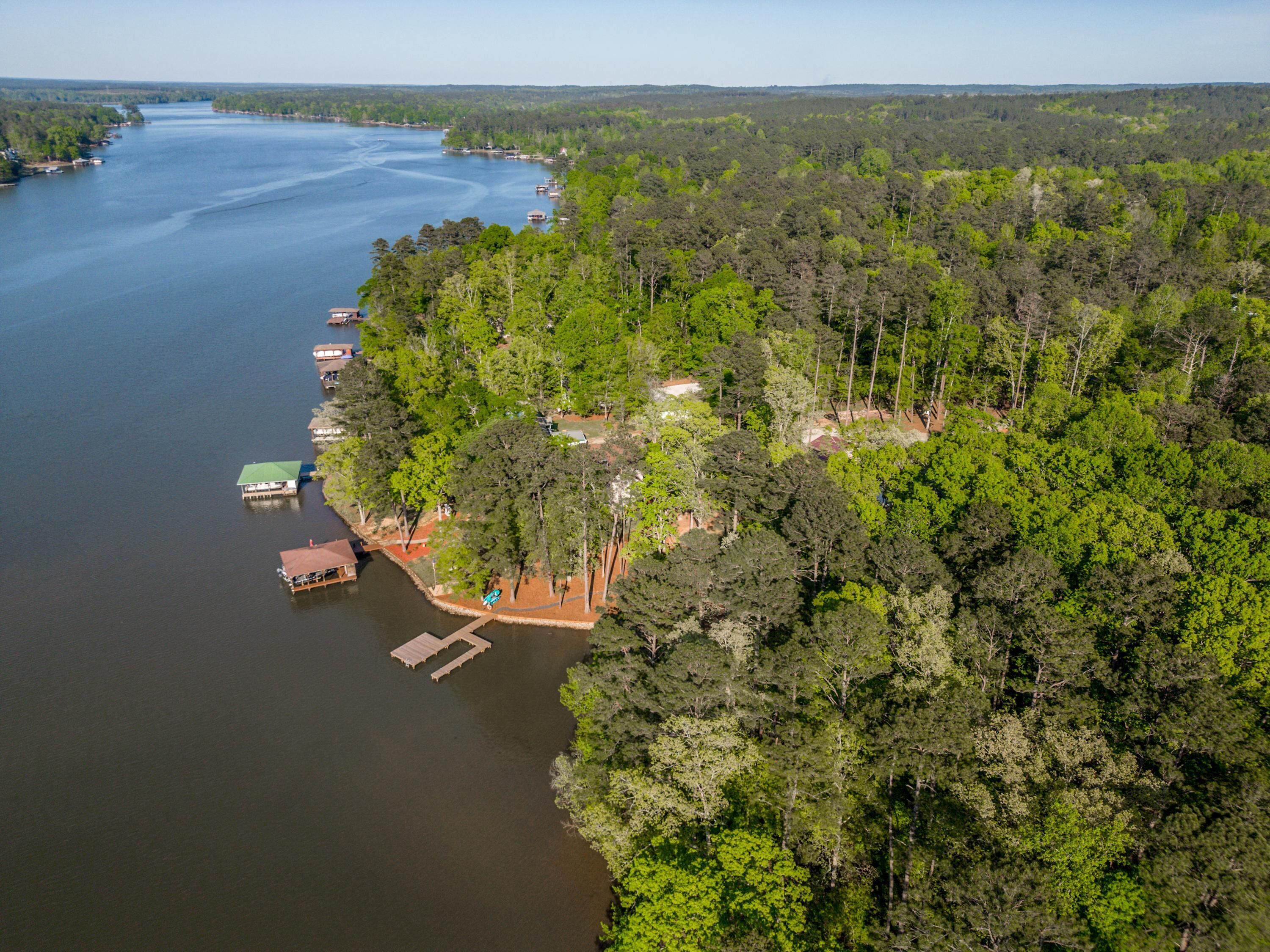 An aerial view of a lakeside property with docked boats, surrounded by dense forest.
