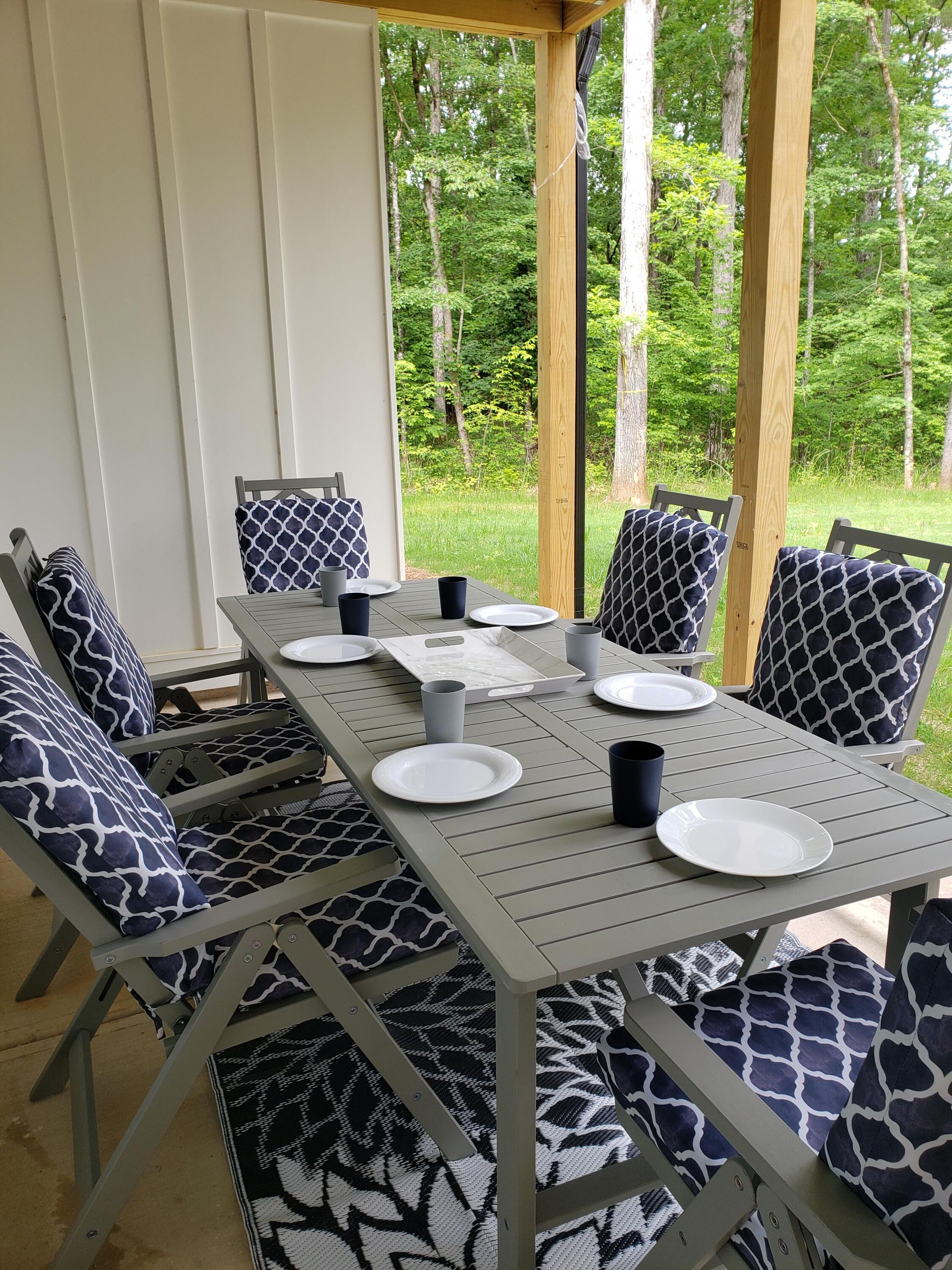 An outdoor patio with a table set for four, surrounded by chairs with patterned cushions.