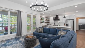 A modern living room with a blue sectional sofa, a grey ottoman, and a chandelier. - Lakefront Bliss - Fully Loaded (Eatonton)