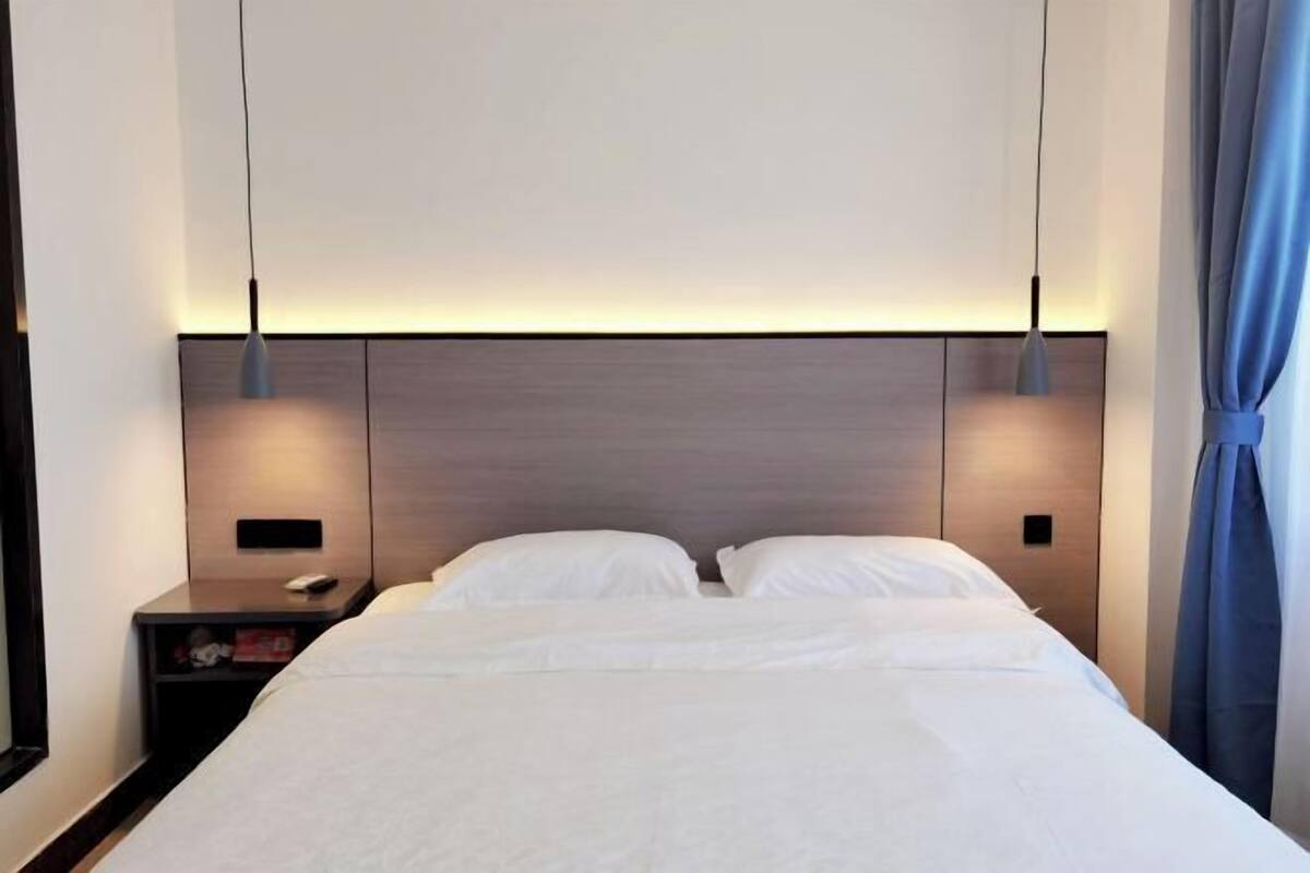 Un lit bien fait, avec du linge de lit blanc, une tête de lit en bois et deux lampes de chevet.