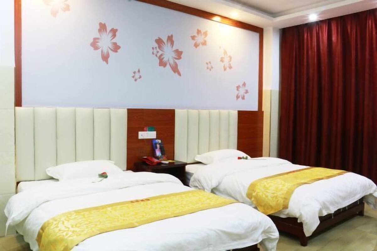 Une chambre d’hôtel avec deux lits, une tête de lit en bois, un mur décoré de motifs floraux et un rideau rouge.