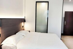 Una habitación de hotel moderna con una cama grande, una mesita de noche, una lámpara de pared y una puerta.