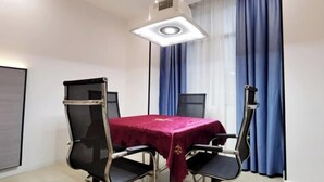 Una sala de conferencias con una mesa, sillas, una lámpara en el techo y cortinas azules.