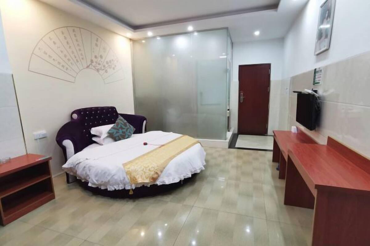 Une chambre à coucher comprenant un lit, une table de chevet, une chaise, un téléviseur et une porte-fenêtre coulissante donnant sur une salle de bain.