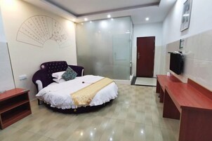 Un dormitorio con cama, mesita de noche, silla, televisor y puerta corredera de vidrio que da a un baño.