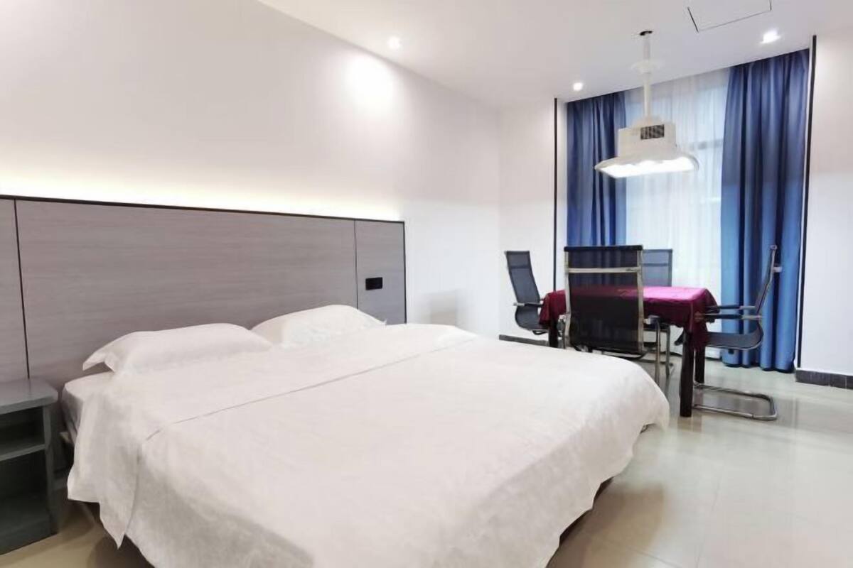 Une chambre d’hôtel avec un grand lit, un bureau avec une chaise, une lampe de bureau et une fenêtre avec des rideaux.