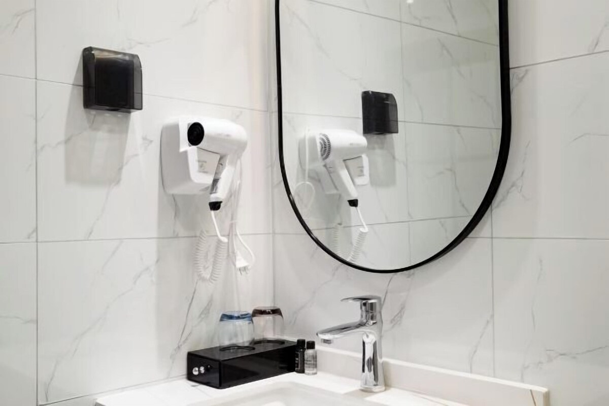 A bathroom with a white sink, a mirror, and two hair dryers mounted on the wall.
