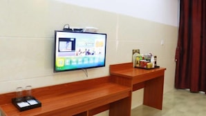 Habitación de hotel con televisor de pantalla plana en la pared, un banco de madera y una mesita con artículos de aseo.
