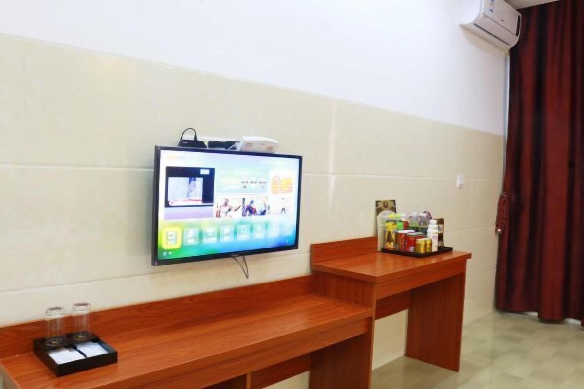 A hotel room with a flat-screen TV mounted on the wall, a wooden bench, and a small table with toiletries.