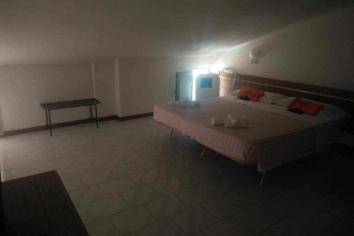 A hotel room with a bed, a bedside table, and a bench in the corner.