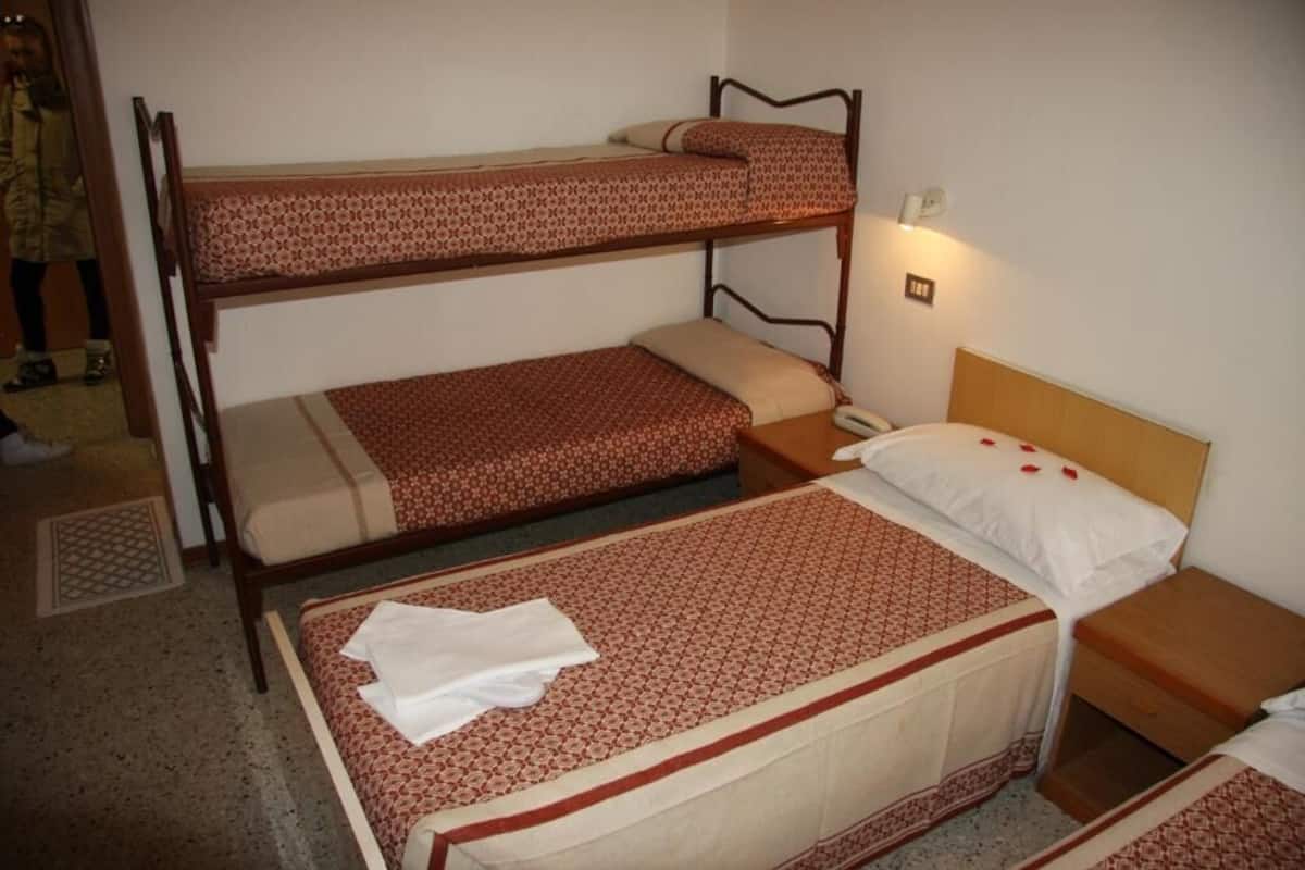 A bunk bed room with a patterned bedspread, a bedside table with a lamp, and a wooden headboard.