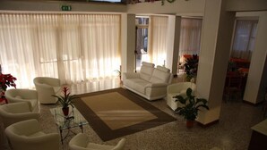 A spacious living area with a white sofa, multiple armchairs, a coffee table, and a rug. - Hotel Orchidea (Rimini)