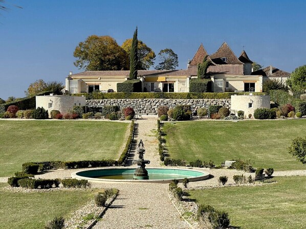 A large, modern house with a symmetrical garden and a central fountain.