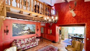 A spacious living room with a large painting, a chandelier, and a red patterned wall. - Elegant Wine Estate: Stunning Views, Heated Pool & Wi-Fi (Fougueyrolles)