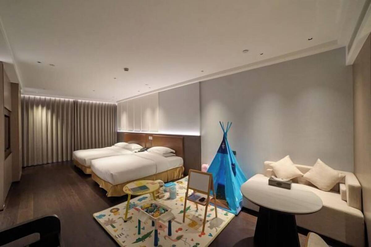 Habitación de hotel con dos camas, un sofá, una mesita, una tienda de campaña y un área de juegos.