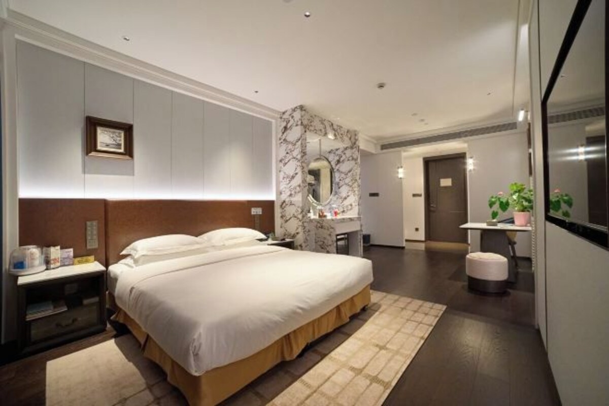 Une chambre d’hôtel moderne dotée d’un grand lit, d’un mur décoratif en marbre, d’un bureau et d’un petit coin salon.