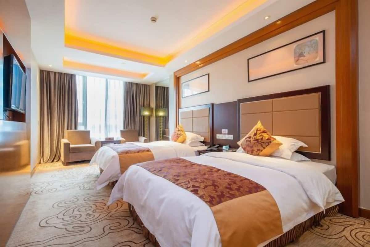 Una habitación de hotel con dos camas, un ventanal grande, una televisión y un escritorio.