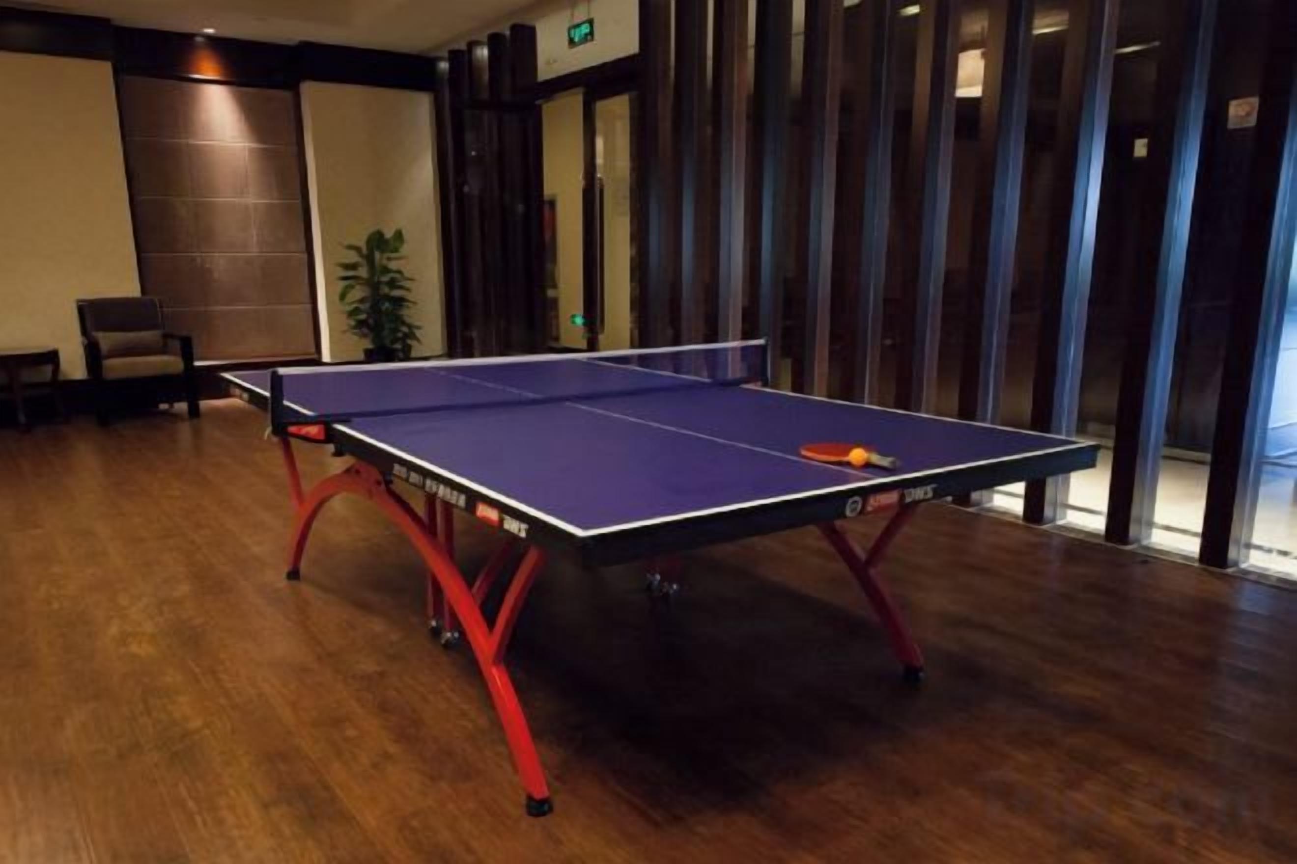 A ping pong table in a room with wooden flooring and a plant in the corner.
