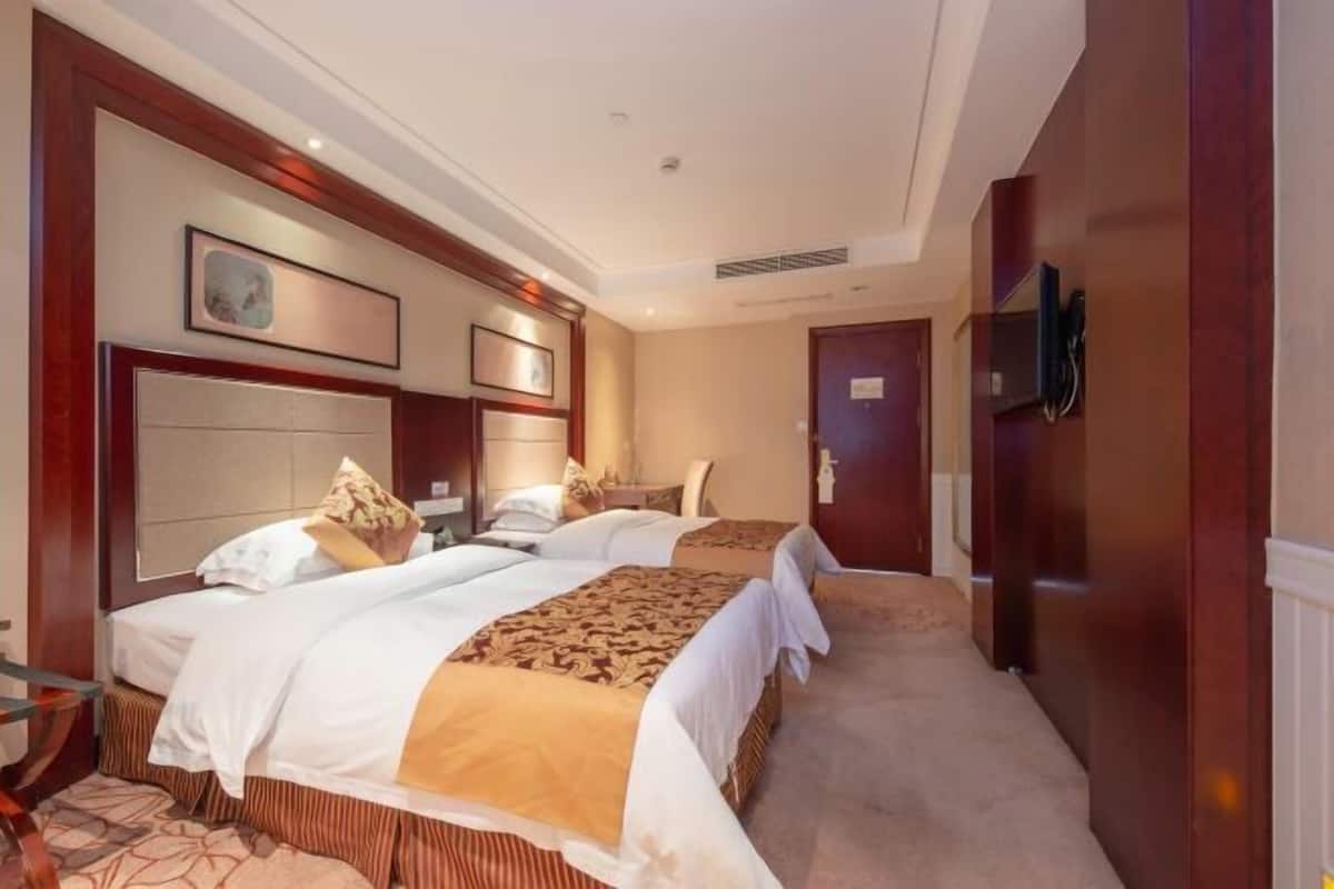 Habitación de hotel con dos camas, un cabecero grande, un televisor de pantalla plana y piso alfombrado.