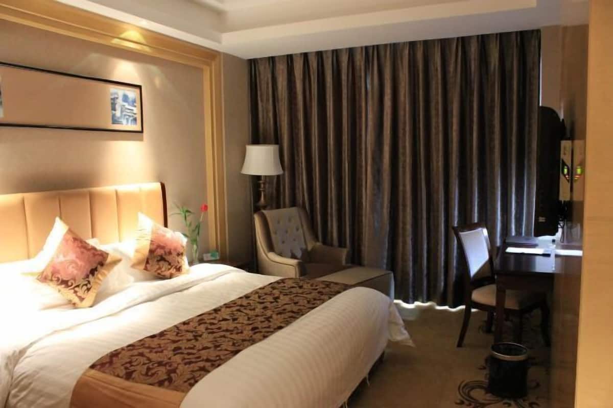 Habitación de hotel con una cama grande, un escritorio, una silla, una lámpara y una cortina.