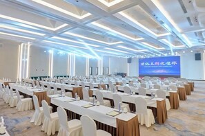 Une salle de conférence avec des rangées de tables et de chaises, un grand écran et un design moderne au niveau du plafond.