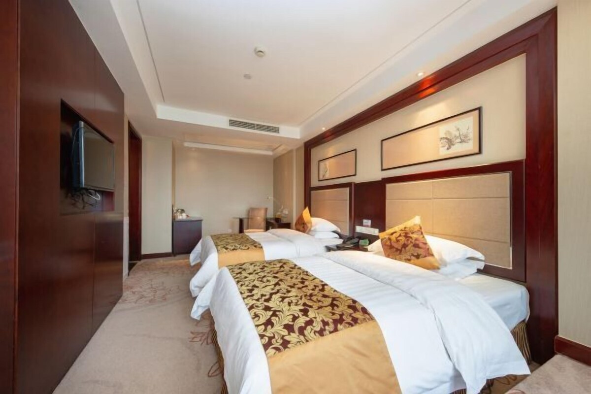 Habitación de hotel con dos camas, un televisor montado en la pared y obras de arte enmarcadas en la cabecera.