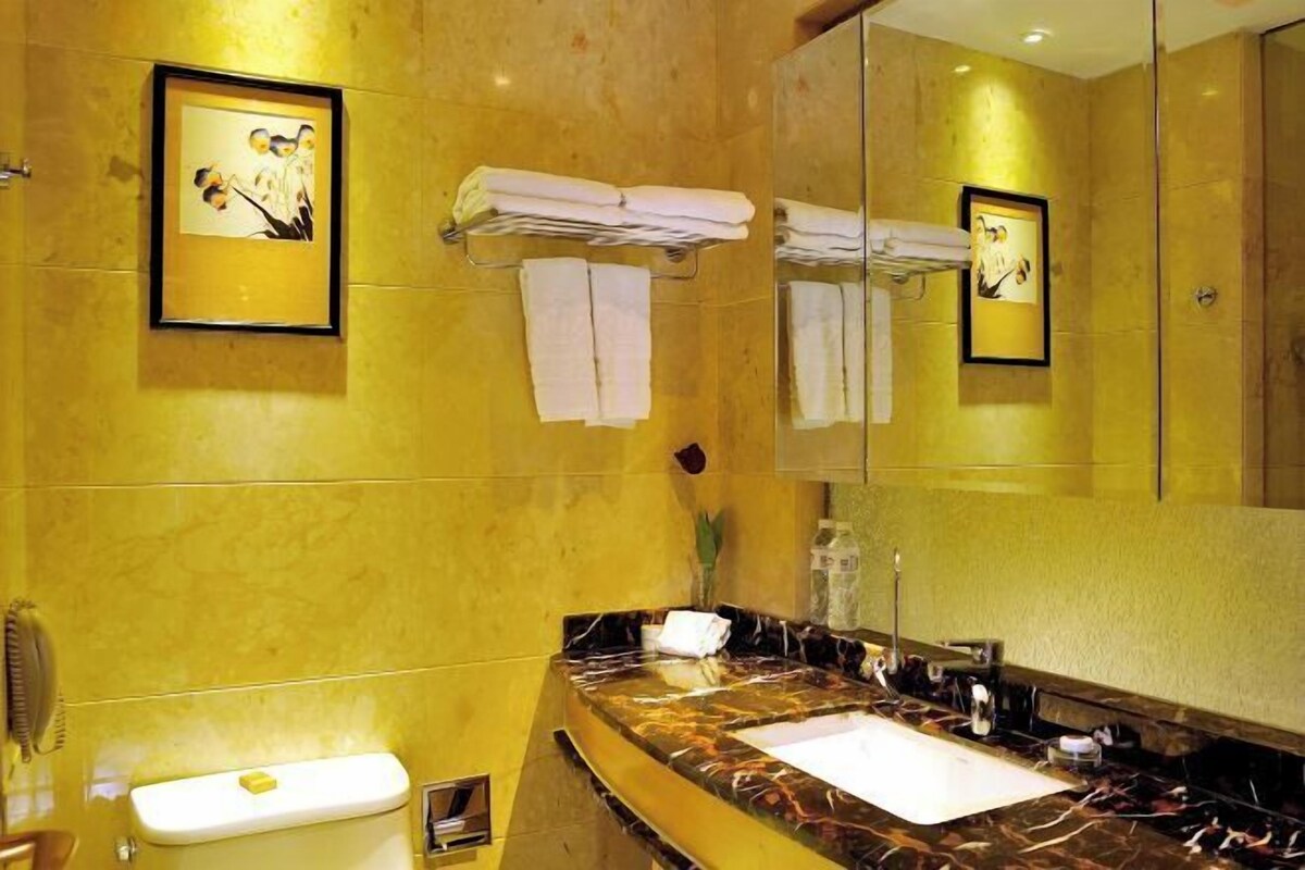 Un baño con lavamanos de mármol, inodoro y espejo. Hay toallas colgadas en un perchero y un cuadro en la pared.
