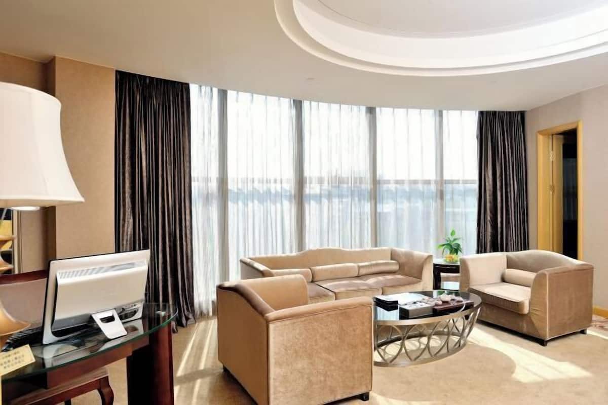 Una habitación de hotel moderna con un ventanal grande, un conjunto de sofás, una mesa de centro y un escritorio con una computadora.