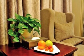 Una habitación con una mesa de madera, una planta en maceta, una caja de pañuelos y un plato con frutas.