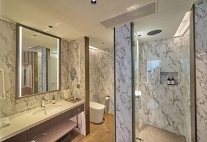 Un baño con pared de mármol, un espejo grande, un lavamanos y un inodoro.