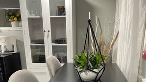 Un comedor con una mesa negra, dos sillas grises, un armario blanco con puertas de vidrio y una planta colgante.