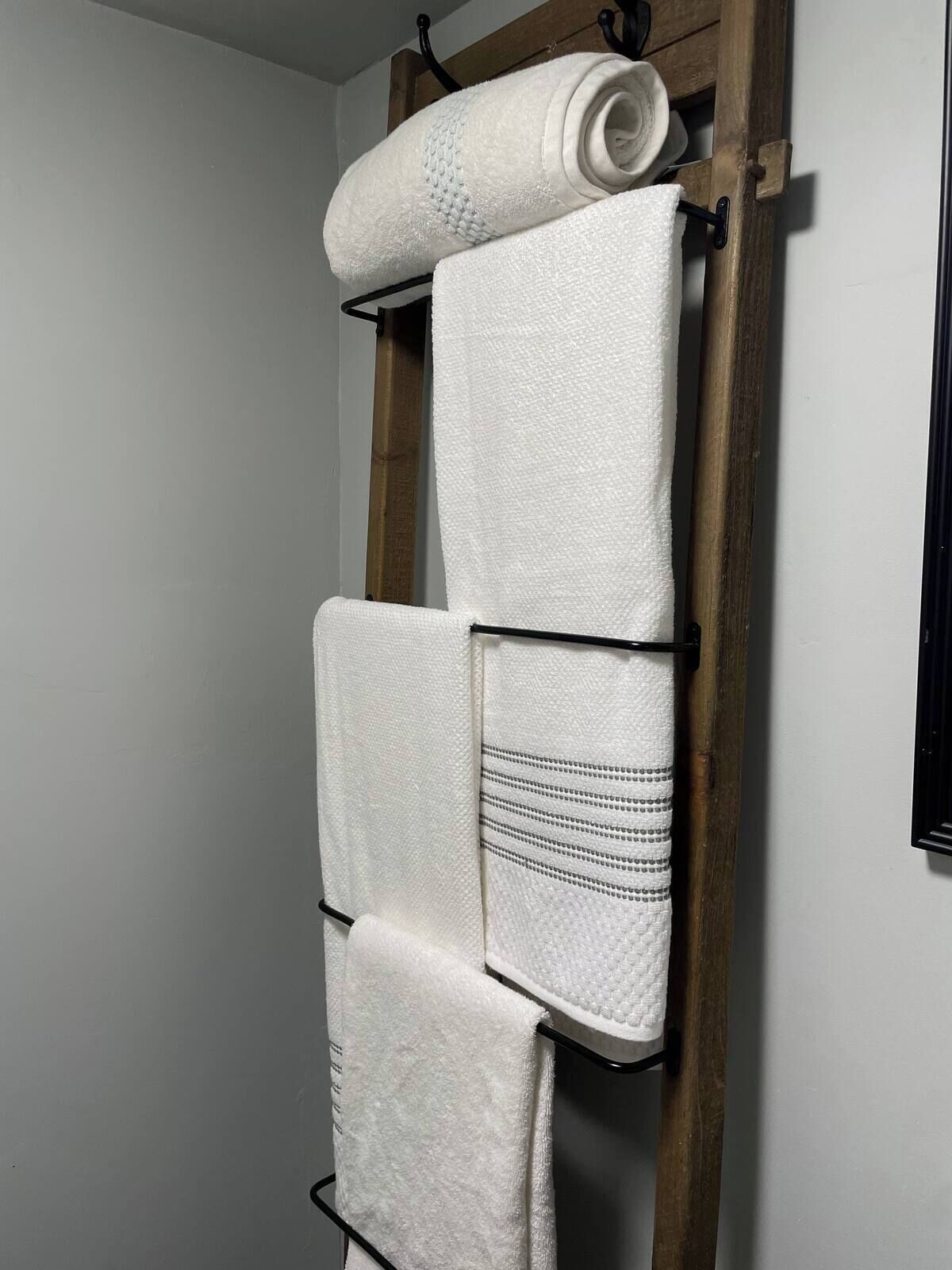 A wooden towel rack with four white towels, one of which has a striped pattern.