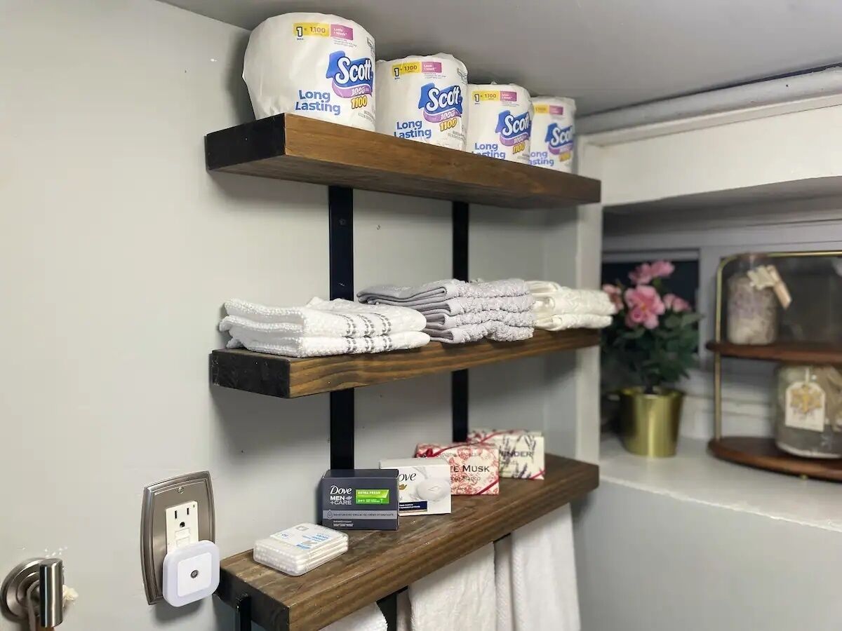 En hyld i badeværelset med toiletpapir, håndklæder og en sæbedispenser.