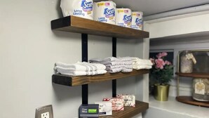 Un estante en el baño con papel higiénico, toallas y dispensador de jabón.