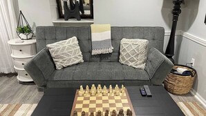 Un tablero de ajedrez sobre una mesa en una sala de estar con un sofá gris y cojines decorativos.
