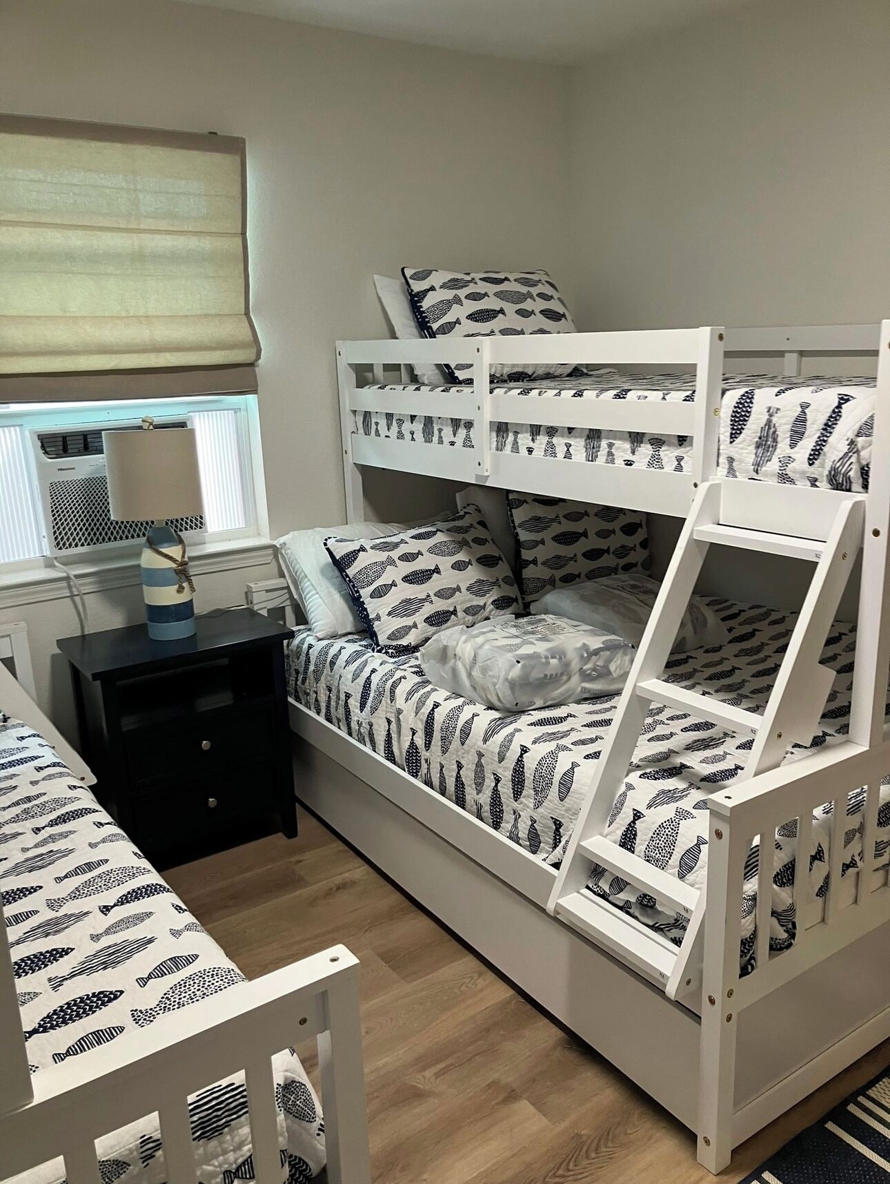 Habitación con literas, una ventana, una mesita de noche y una cama con colcha estampada.