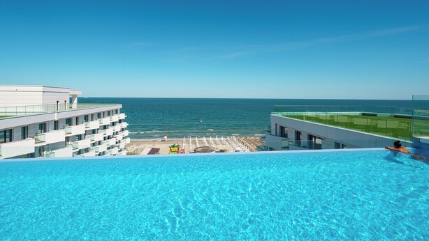 A hotel with a pool overlooking the sea, a beach, and a clear sky. - ROYALE SUNDANCE 225 INFINITY (Navodari)