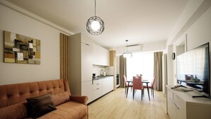 A modern living room with a sofa, a dining area with chairs, a kitchen with cabinets, and a TV on a stand. - ROYALE SUNDANCE 225 INFINITY (Navodari)