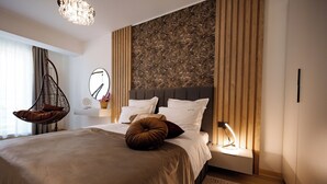 A modern bedroom with a large bed, a hanging chair, a bedside table with a lamp, and a decorative wall panel. - ROYALE SUNDANCE 225 INFINITY (Navodari)