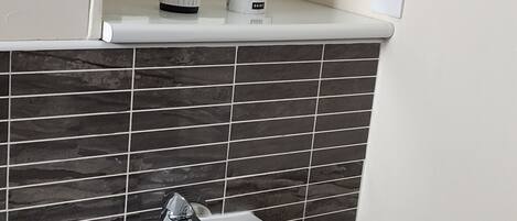 Un baño con lavamanos blanco, un espejo y un salpicadero de azulejos.
